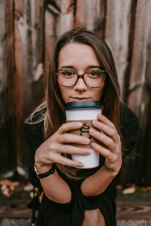 A woman drinking a cup of coffee, wearing tortoiseshell-patterned glasses.